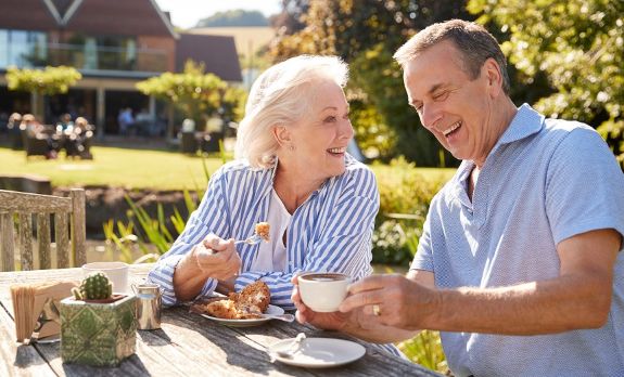 Two confident investors who are about to retire relax while sipping coffee and eating brunch outdoors.