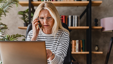 A woman looking at a laptop while talking on a mobile phone